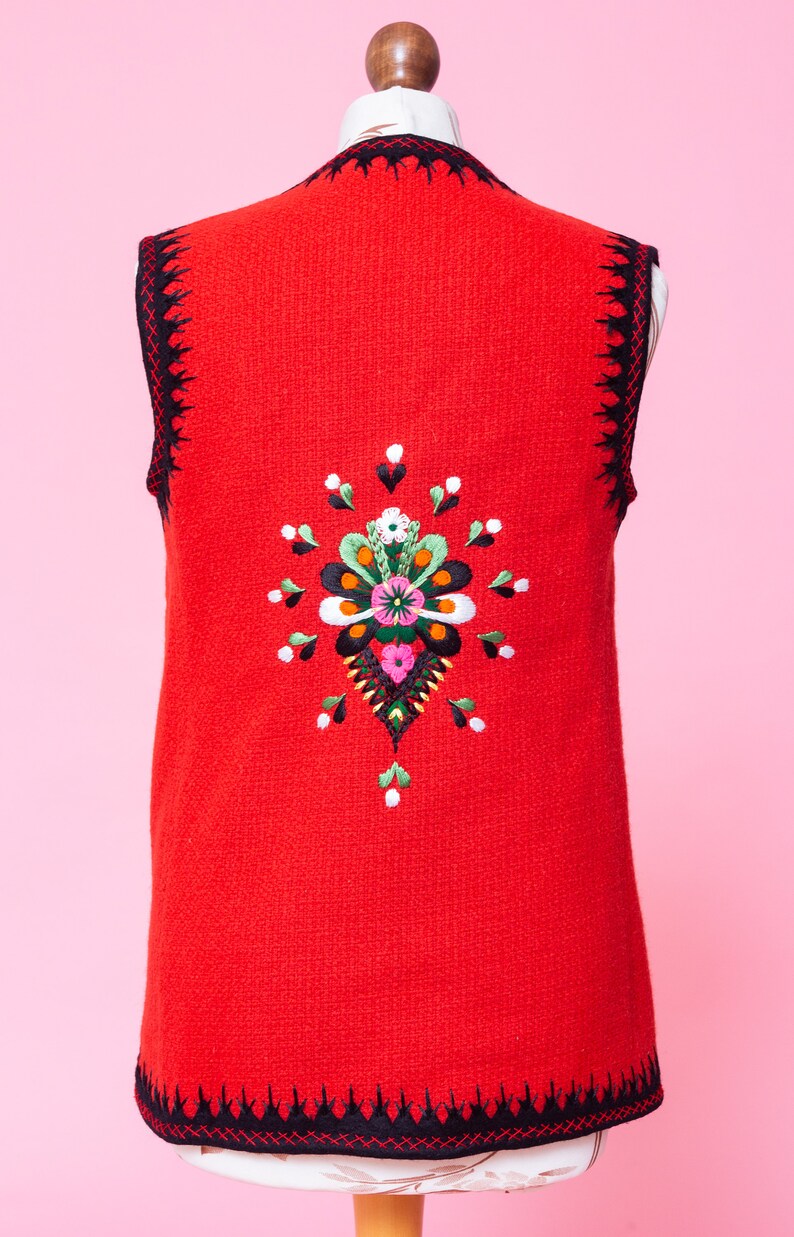 Pode incluir: Um colete vermelho sem mangas com acabamento preto e um design floral bordado colorido nas costas.