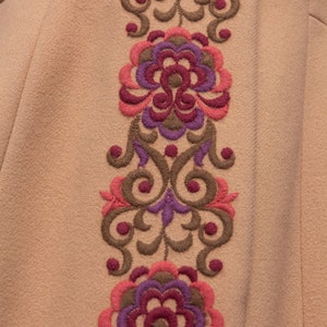 May include: A beige fabric with a brown, pink, and purple embroidered floral design.