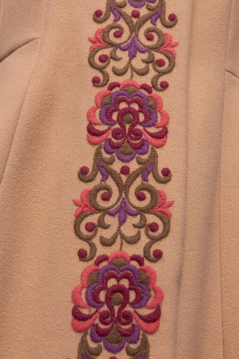 May include: A beige fabric with a brown, pink, and purple embroidered floral design.
