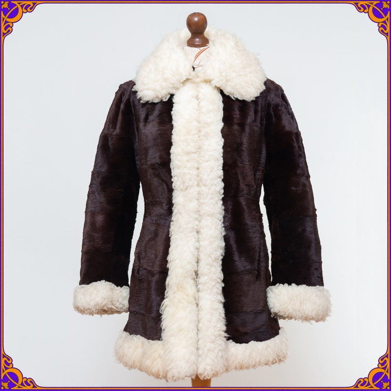 May include: A brown faux fur coat with a white faux fur collar and trim. The coat has a long, fitted silhouette and a zipper closure.