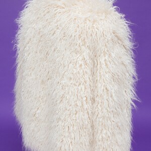 May include: A white fluffy faux fur jacket on a mannequin. The jacket has a long, loose fit and a soft, plush texture.