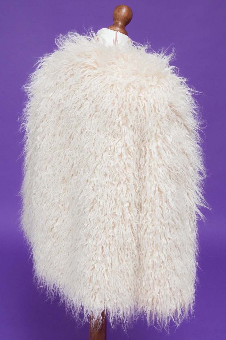 May include: A white fluffy faux fur jacket on a mannequin. The jacket has a long, loose fit and a soft, plush texture.