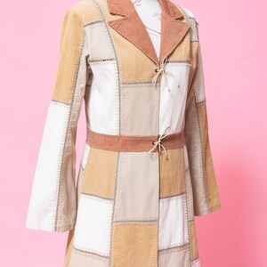 K&ouml;nnte beinhalten: Eine lange Patchworkjacke mit einem braunen Cordkragen und einem braunen G&uuml;rtel. Die Jacke ist aus verschiedenen Beige- und Wei&szlig;t&ouml;nen aus Cord gefertigt.