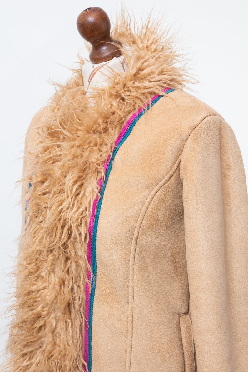 May include: A tan suede jacket with a faux fur collar. The jacket has a pink and teal trim along the front zipper.