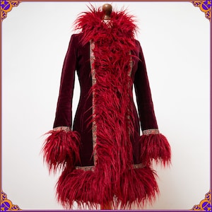 Peut inclure: Un manteau en velours bordeaux avec une garniture en fausse fourrure rouge vif. Le manteau présente un col haut, des poignets et un panneau central en fourrure. Des détails brodés complexes ornent les bords, créant un vêtement saisissant d'inspiration bohème.