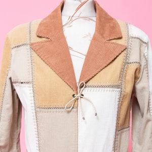 K&ouml;nnte beinhalten: Eine Patchwork-Jacke aus Cord in Braun, Beige und Wei&szlig;. Die Jacke hat einen Bindeverschluss vorne und einen braunen Cordg&uuml;rtel.