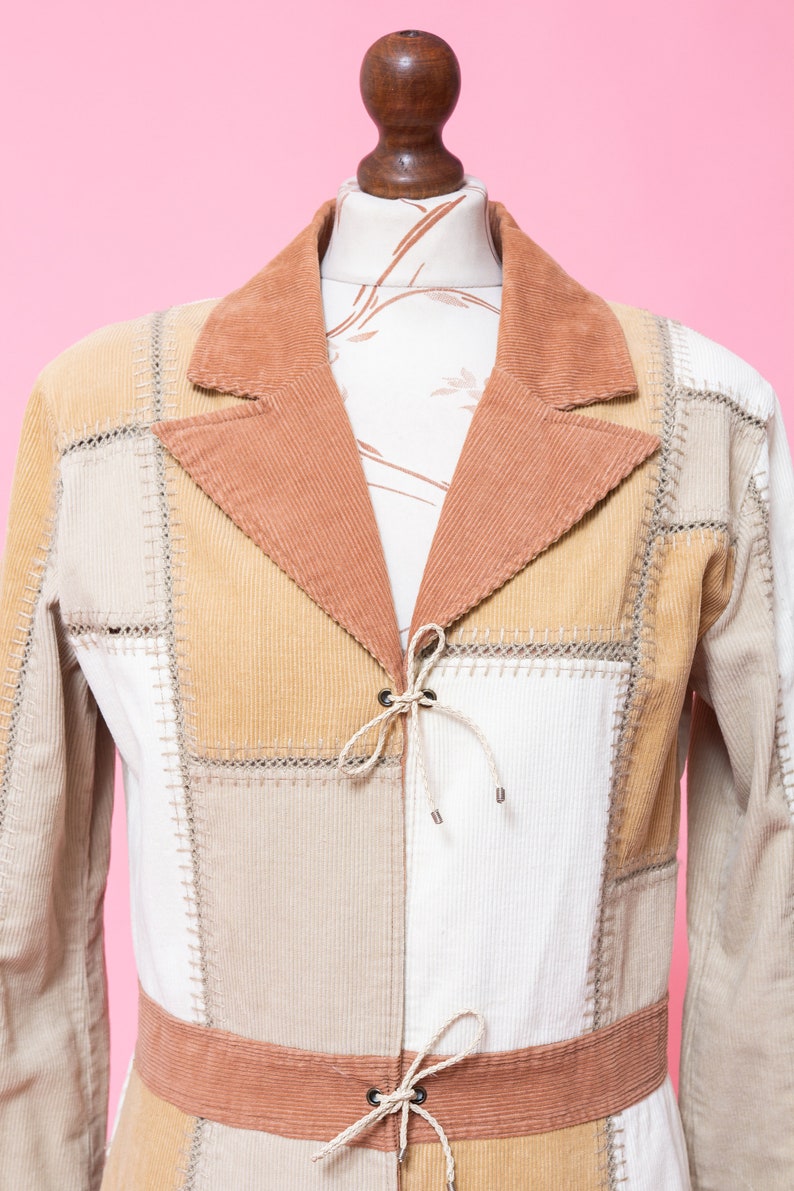 K&ouml;nnte beinhalten: Eine Patchwork-Jacke aus Cord in Braun, Beige und Wei&szlig;. Die Jacke hat einen Bindeverschluss vorne und einen braunen Cordg&uuml;rtel.