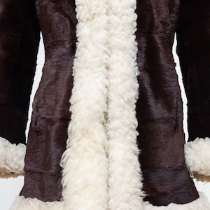 May include: A brown faux fur coat with a white sherpa lining. The coat has a long, fitted silhouette and a collar.