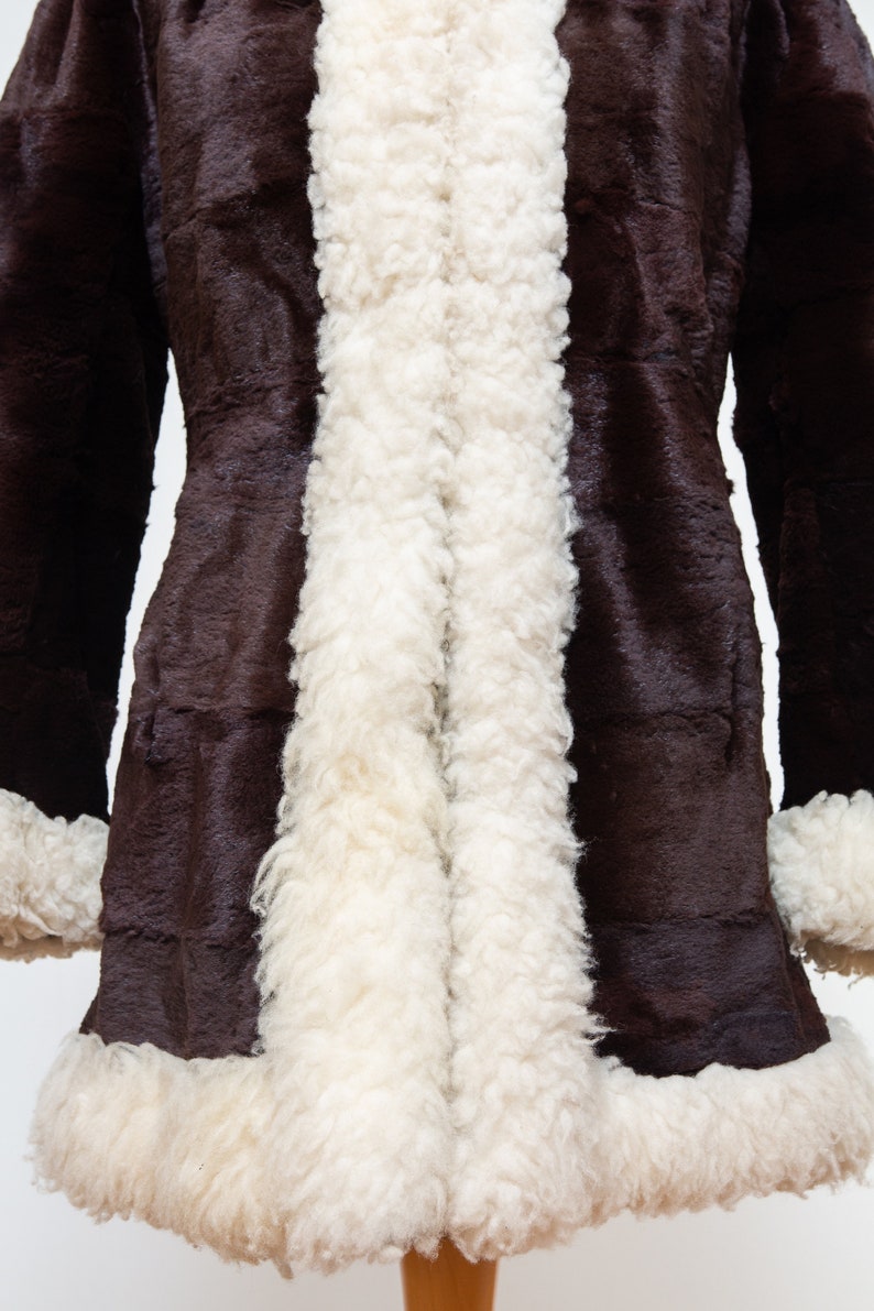 May include: A brown faux fur coat with a white sherpa lining. The coat has a long, fitted silhouette and a collar.