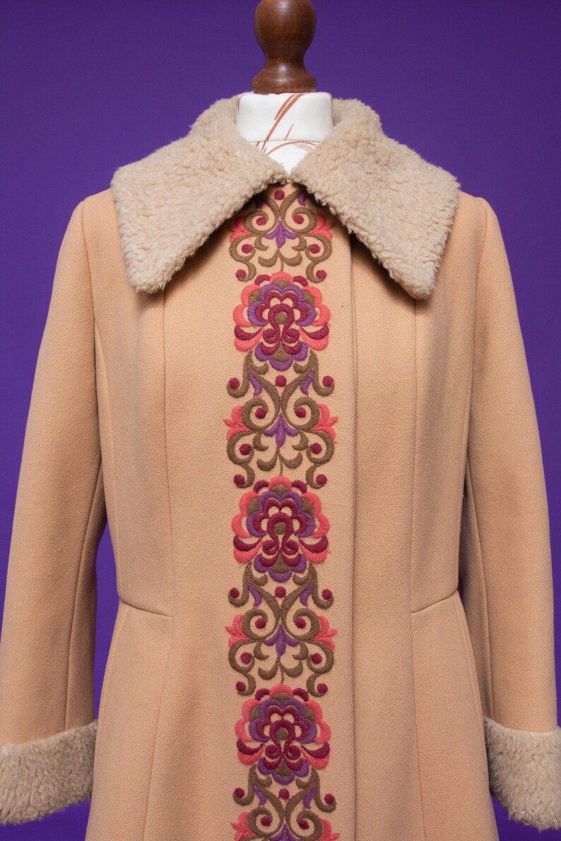 May include: A tan long coat with a faux fur collar and a floral embroidered design down the front.