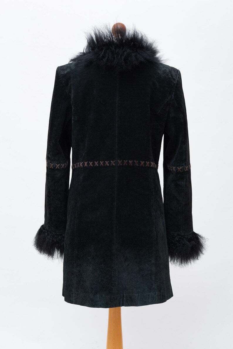 May include: A black coat with a faux fur collar and cuffs. The coat features decorative stitching across the waist and on the sleeves. The coat is displayed on a wooden hanger against a white background. The coat is a knee-length style.