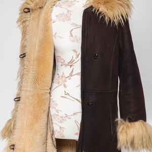 May include: A vintage brown shearling coat with a tan fur collar and cuffs. The coat is buttoned and displayed on a mannequin. The interior lining is a light tan color, and the exterior is a dark brown. The coat has a classic, retro style.