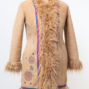 May include: A tan suede coat with a faux fur collar and lining. The coat has a pink and teal trim and embroidered geometric designs.