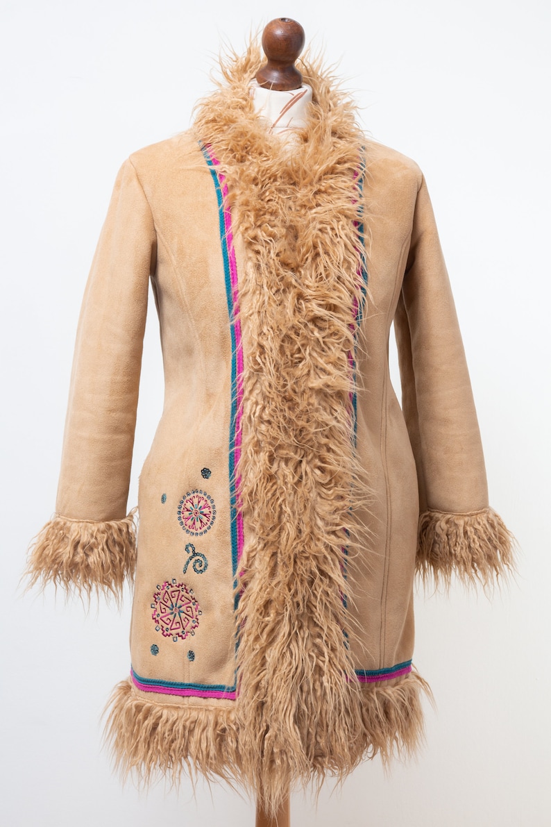 May include: A tan suede coat with a faux fur collar and lining. The coat has a pink and teal trim and embroidered geometric designs.