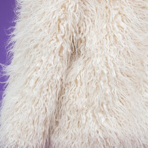 May include: A white faux fur jacket with a soft, fluffy texture. The jacket is displayed on a purple background.