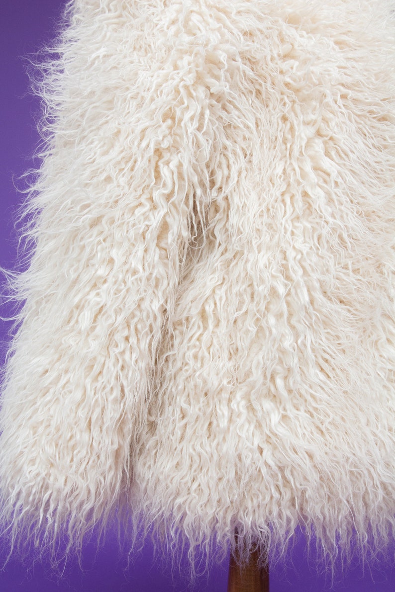 May include: A white faux fur jacket with a soft, fluffy texture. The jacket is displayed on a purple background.