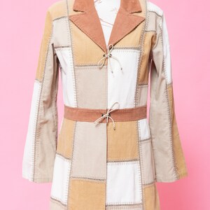 K&ouml;nnte beinhalten: Eine lang&auml;rmelige Patchworkjacke mit braunem Cordkragen und G&uuml;rtel. Die Jacke ist aus beigefarbenem, braunem und wei&szlig;em Stoff.