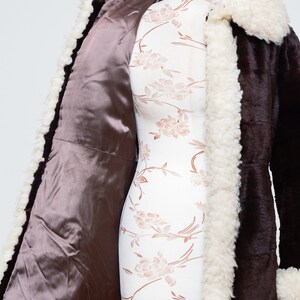 May include: A brown faux fur coat with a white faux fur collar and lining. The coat is open and the lining is visible.