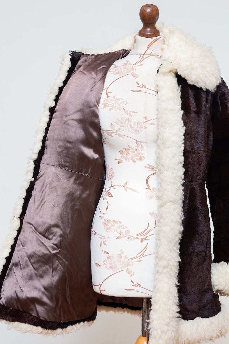 May include: A brown faux fur coat with a white faux fur collar and lining. The coat is open and the lining is visible.