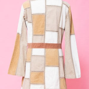 K&ouml;nnte beinhalten: Eine Patchworkjacke mit braunem Cordkragen und G&uuml;rtel. Die Jacke ist aus beigefarbenem und wei&szlig;em Cord und hat ein quadratisches Patchworkmuster.