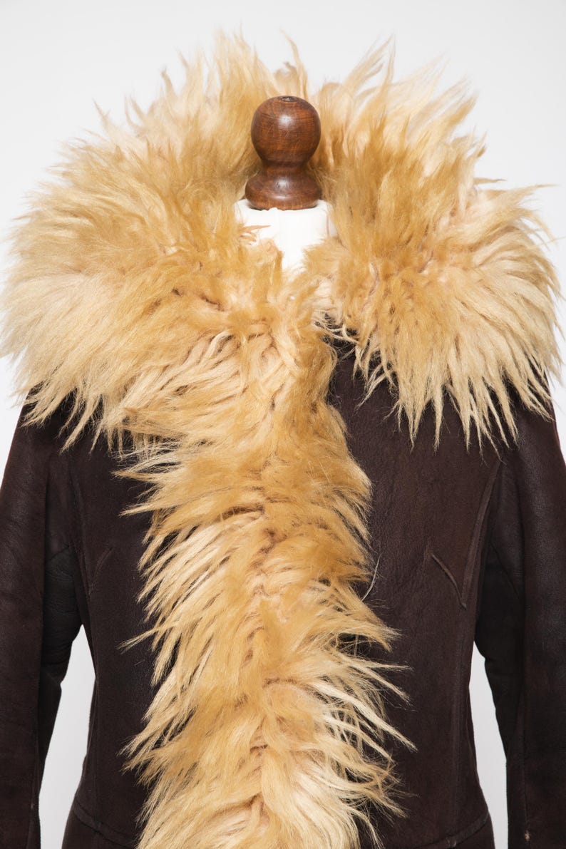 May include: A dark brown coat with a tan fur collar. The coat has a classic design with a plush, textured fur collar that frames the neckline. The fur is a light tan color, contrasting with the dark brown of the coat.