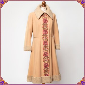 May include: A long, beige coat with a brown faux fur collar and a floral embroidered design down the front.