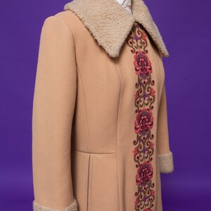May include: A long, tan coat with a large, fluffy collar and a decorative embroidered floral pattern down the front.