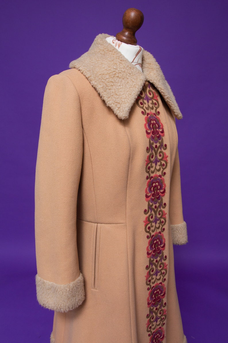 May include: A long, tan coat with a large, fluffy collar and a decorative embroidered floral pattern down the front.