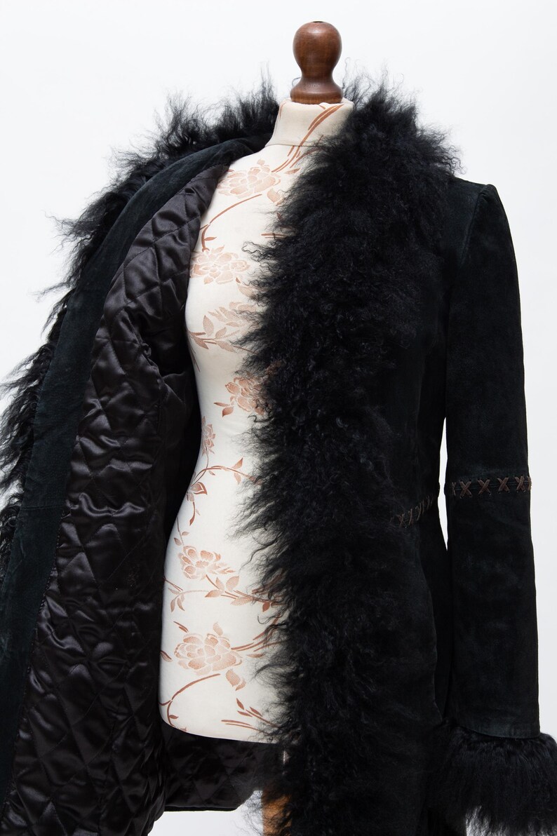 May include: Black suede coat with a faux fur trim and lining. The coat features a quilted interior and decorative stitching on the sleeves. The coat is displayed on a mannequin.