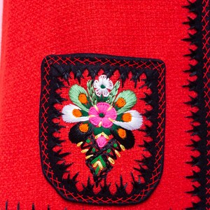 Pode incluir: Tecido vermelho com acabamento bordado preto e um desenho floral no centro do tecido. O desenho floral &eacute; bordado em tons de rosa, verde, branco e laranja.