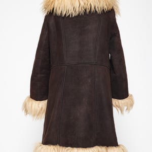 May include: A dark brown coat with a light brown fur collar, cuffs, and hem. The coat has a long length and a classic design, perfect for cold weather. The coat is made of a soft, suede-like material.