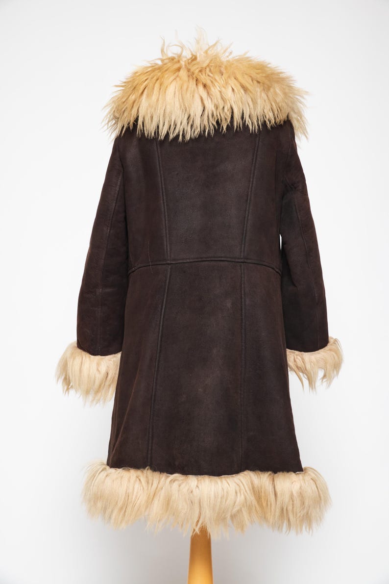 May include: A dark brown coat with a light brown fur collar, cuffs, and hem. The coat has a long length and a classic design, perfect for cold weather. The coat is made of a soft, suede-like material.