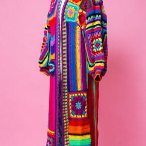 K&ouml;nnte beinhalten: Lange, bunte H&auml;keljacke auf einer Schaufensterpuppe. Das Kleidungsst&uuml;ck hat ein Patchwork-Design mit Quadraten und Streifen in Rot, Orange, Gelb, Gr&uuml;n, Blau und Lila. Es hat lange &Auml;rmel und einen Kragen.
