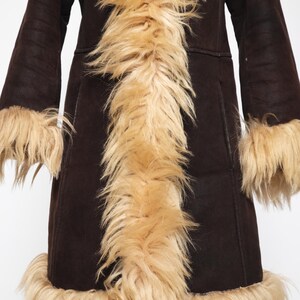 May include: A dark brown coat with long sleeves and a faux fur trim. The coat features a light brown faux fur collar, cuffs, and hem. The coat is displayed on a wooden stand against a white background.