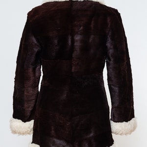 May include: A brown faux fur coat with a white faux fur collar and trim. The coat has a long, fitted silhouette and is lined with white faux fur.