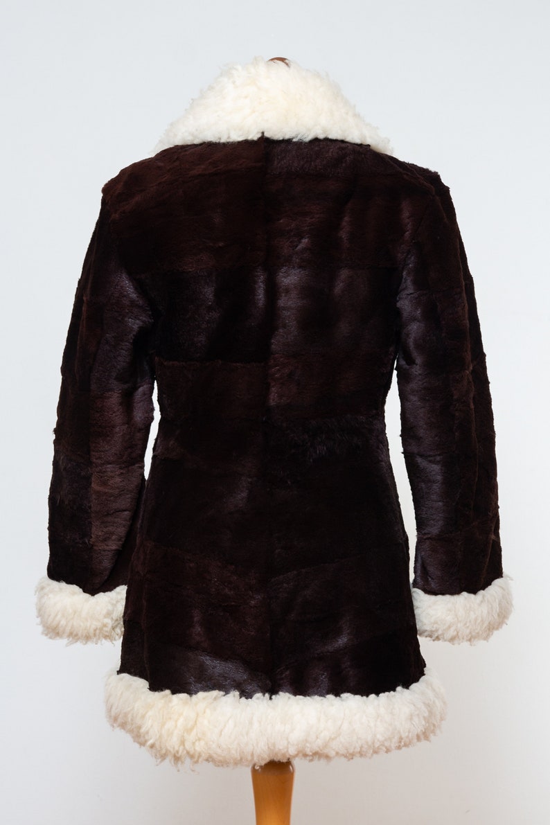 May include: A brown faux fur coat with a white faux fur collar and trim. The coat has a long, fitted silhouette and is lined with white faux fur.