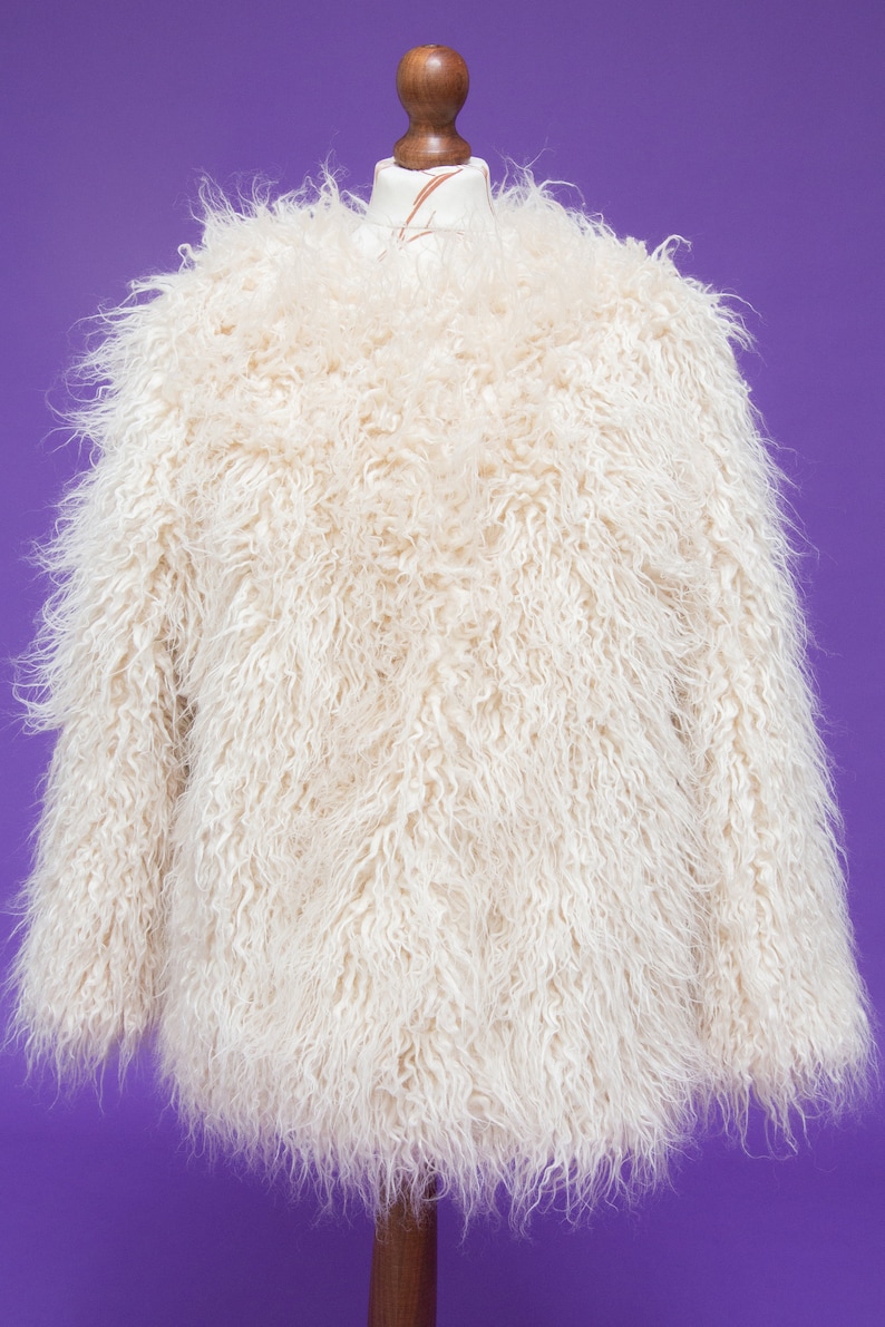 May include: A white faux fur jacket with a long, shaggy pile. The jacket is on a mannequin and has a relaxed fit.