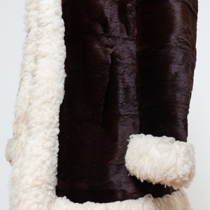 May include: A brown faux fur coat with a white shearling lining and trim. The coat has a long sleeve and a classic style.