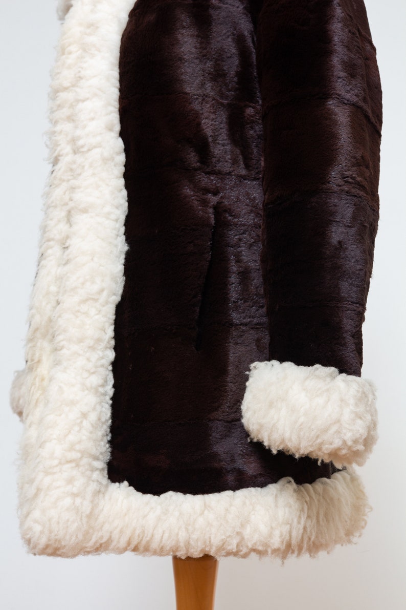 May include: A brown faux fur coat with a white shearling lining and trim. The coat has a long sleeve and a classic style.