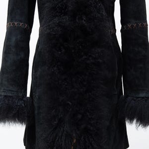May include: A black suede coat with a fur-lined collar, cuffs, and front. The coat features decorative stitching on the sleeves and waist. The coat is a mid-length design.