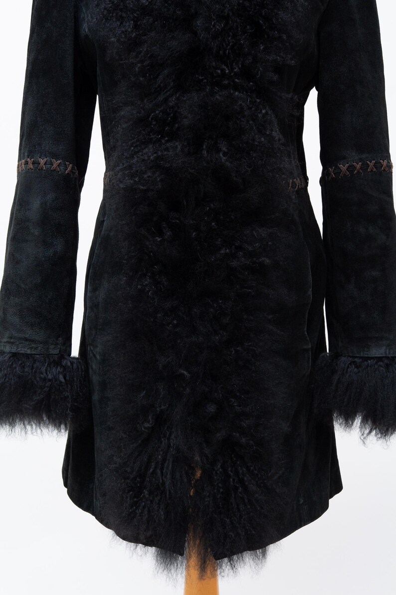 May include: A black suede coat with a fur-lined collar, cuffs, and front. The coat features decorative stitching on the sleeves and waist. The coat is a mid-length design.