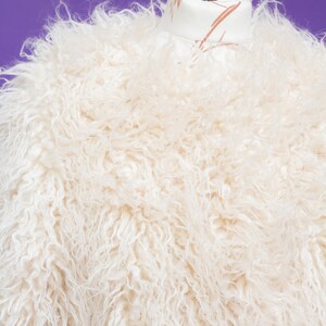 May include: A white fluffy faux fur jacket on a mannequin. The jacket has a soft, plush texture.