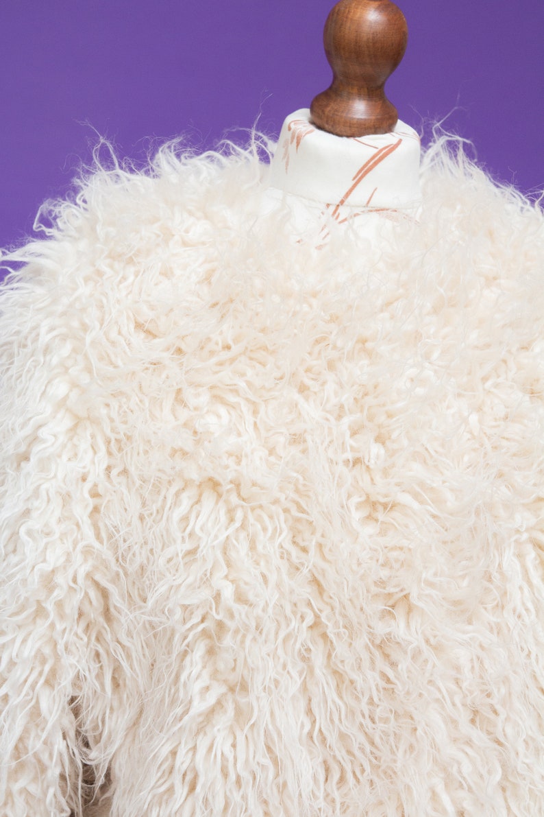 May include: A white fluffy faux fur jacket on a mannequin. The jacket has a soft, plush texture.