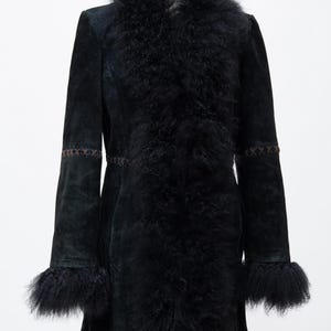 May include: A black suede coat with a faux fur collar and cuffs. The coat features decorative stitching on the sleeves and a tailored fit. The coat is displayed on a mannequin against a white background.