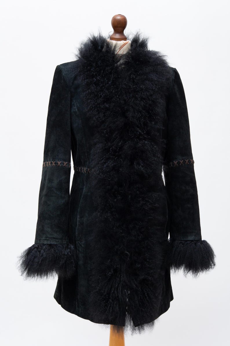 May include: A black suede coat with a faux fur collar and cuffs. The coat features decorative stitching on the sleeves and a tailored fit. The coat is displayed on a mannequin against a white background.