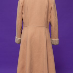 May include: A long, light brown coat with a fluffy white collar and cuffs. The coat has a fitted bodice and a flared skirt.