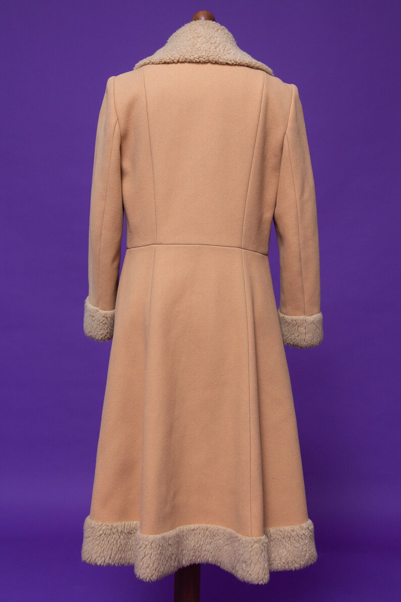 May include: A long, light brown coat with a fluffy white collar and cuffs. The coat has a fitted bodice and a flared skirt.
