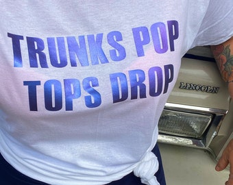 Op de afbeelding: Wit T-shirt met een blauwe en paarse iriserende afbeelding met de tekst "TRUNKS POP TOPS DROP".
