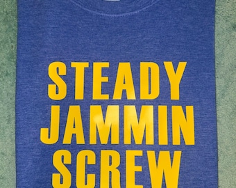 Op de afbeelding: Een blauw T-shirt met de tekst "STEADY JAMMIN SCREW" in het geel.