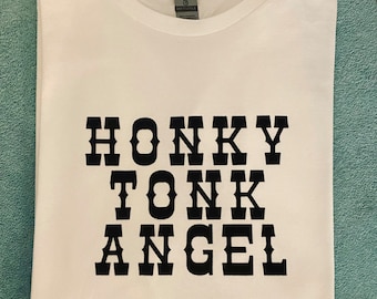 Op de afbeelding: Wit T-shirt met zwarte tekst die "Honky Tonk Angel" luidt.
